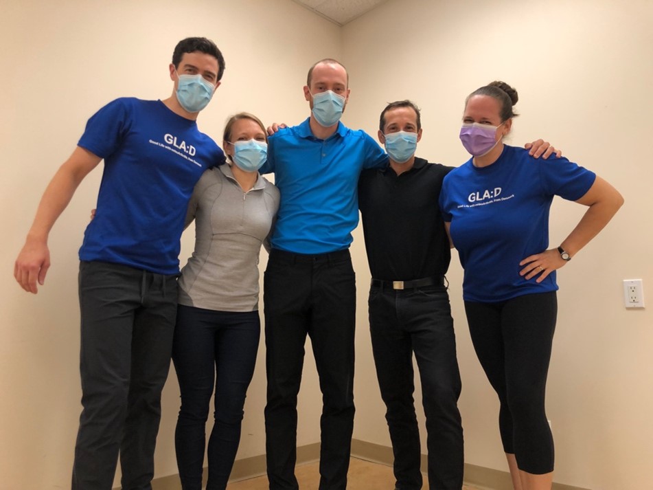 Five physios stand with arms around each others' shoulders, masked and smiling