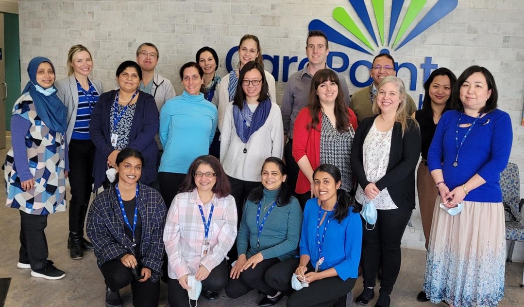 A large group of CarePoint Health staff stand in front of their logo in thier building